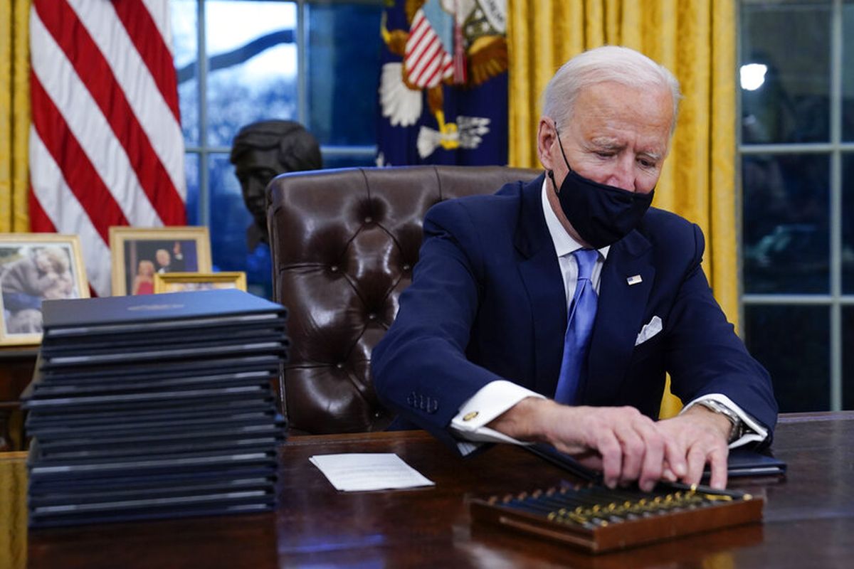 President Joe Biden reaches for a pen to sign his first executive order in the Oval Office of the White House on Wednesday, Jan. 20, 2021, in Washington. (AP Photo/Evan Vucci)