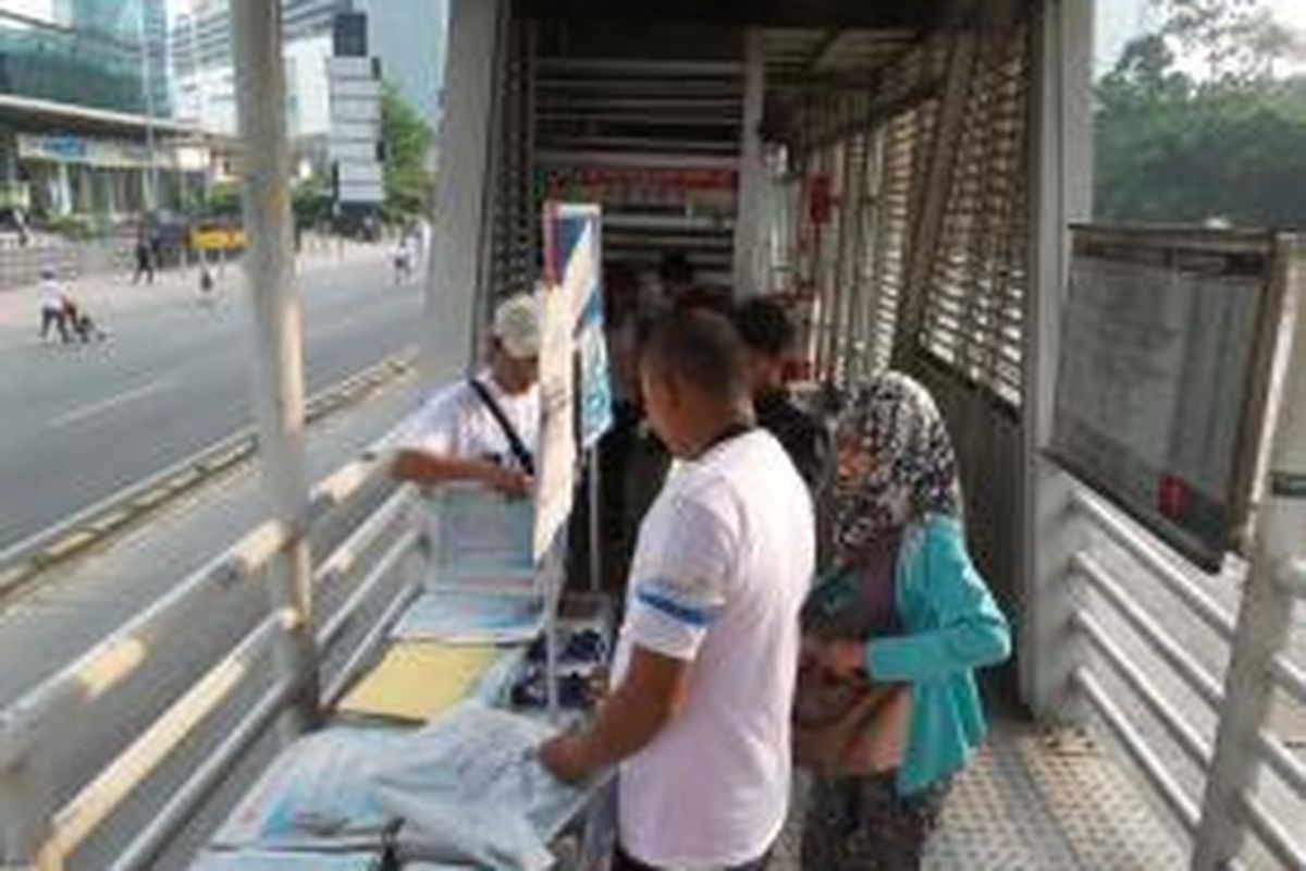 Seorang pengguna transjakarta membeli koran Kompas di outlet Halte Tosari ICBC, Minggu (28/6/2015). Harian Kompas memberikan hadiah kepada para pengguna bus transjakarta dan penggemar film dalam rangka ulang tahunnya yang ke-50. Hadiah itu berupa naik transjakarta dan nonton film di XXI hanya dengan membayar Rp 50.  