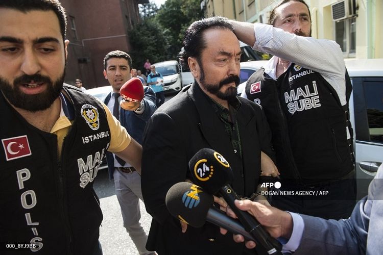 Foto arsip yang diambil pada 11 Juli 2018 saat petugas polisi Turki mengawal televangelis dan pemimpin sekte, Adnan Oktar (tengah) alias Harun Yahya di Istanbul, saat dia ditangkap atas tuduhan penipuan. Dia terbukti telah melakukan kejahatan seksual yang mengakibatkannya dipenjara lebih dari 1.000 tahun.