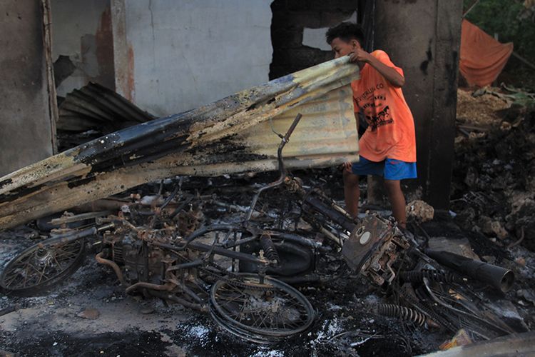 Seorang warga berada di bangkai dua unit sepeda motornya yang terbakar di dalam rumahnya pasca-keributan antar pemuda di Desa Gunung Jaya, Buton, Sulawesi Tenggara, Kamis (6/6/2019).  Pihak kepolisian belum mengetahui jumlah kendaraan yang terbakar pasca-kejadian pembakaran 87 unit rumah di Desa Gunung Jaya sementara Pemerintah Kabupaten Buton juga belum merinci jumlah kerugian materiil akibat kejadian tersebut.