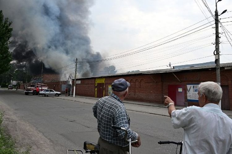 Para penduduk melihat asap membumbung dari pasar pusat Kota Sloviansk, utara Kramatosk pada 5 Juli 2022, menyusul dugaan serangan rudal di tengah invasi Rusia ke Ukraina.