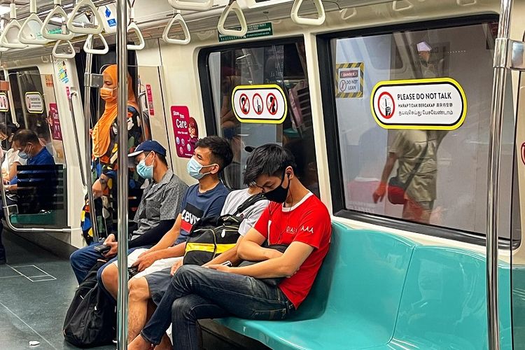 Pengumuman dilarang berbicara di MRT Singapura untuk mencegah penyebaran virus Covid-19 tertempel di jendela dekat kursi penumpang yang sedang duduk ketika MRT melintas di Central Business District (CBD) Raffles Place, Rabu siang (17/11/2021)