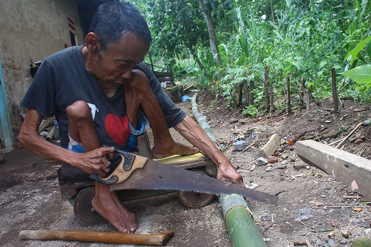 Turiyan (57) saat memotong bambu untuk dijadikan tampah di rumahnya di RT 41 RW 7 Dusun Lepur, Desa Jambangan, Kecamatan Dampit, Kabupaten Malang, Minggu (8/3/2020). Turiyan mengalami cacat fisik berupa kelumpuhan akibat jatuh tertimpa batu di sungai saat masih duduk di kelas 2 SD dan membuatnya harus berjalan menggunakan mobil mainan dari kayu.