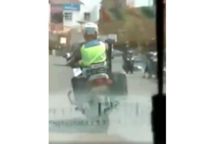 Tangkapan layar video yang menampilkan seorang anggota polisi lalu lintas sedang mengawal mobil ambulans yang sirinenya rusak.