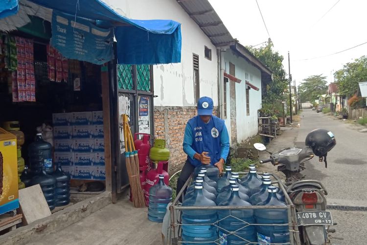 Junaidi mengangkat air galon dari becak motornya ke warung pelanggan, Senin (27/11/2023) di Padang.