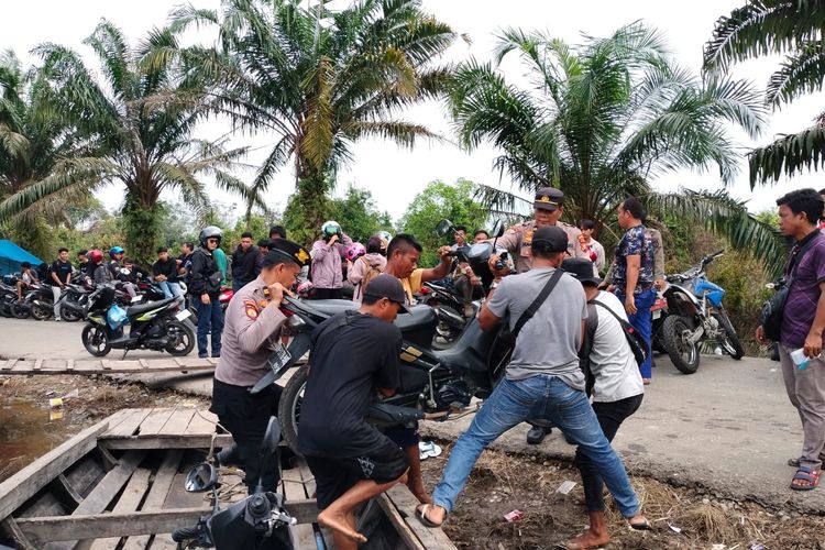 Petugas kepolisian menolong warga menaikkan sepeda motor ke dalam pompong untuk melewati genangan banjir, di Kelurahan Kerinci Kota, Kecamatan Pangkalan Kerinci, Kabupaten Pelalawan, Riau, Jumat (26/1/2024).