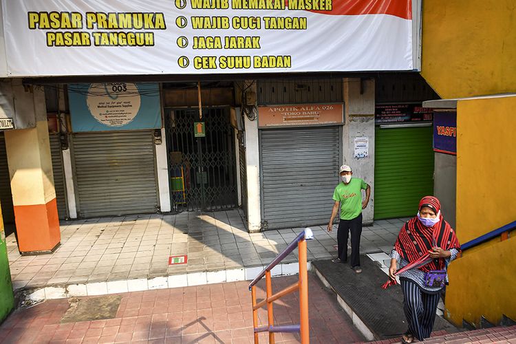 Warga berjalan di depan toko yang tutup di Pasar Pramuka, Jakarta, Minggu (12/7/2020). Pengelola Pasar Pramuka menutup sementara pasar tersebut dari Sabtu (11/7) hingga Senin (13/7) menyusul satu orang pedagang terkonfirmasi positif COVID-19 setelah melakukan tes usap secara mandiri.