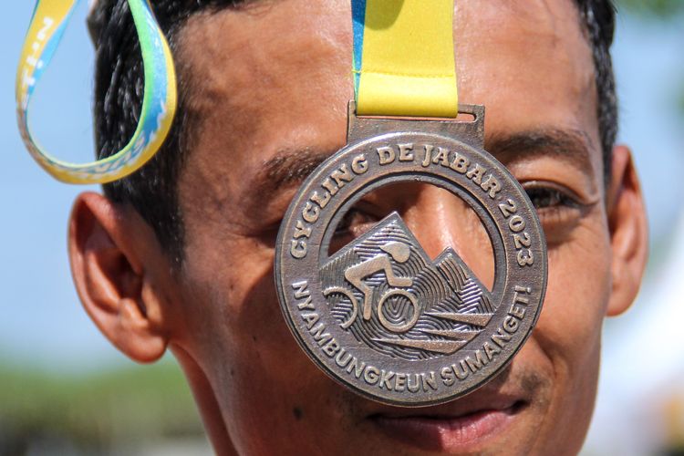 Salah seorang pemenang Cycling de Jabar 2023 kategori Men non-Elite Rafika Farisi dengan medalinya yang ia perlihatkan seusai finis di Paamprokan Pangandaran, Minggu (9/7/2023).