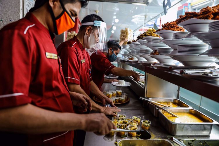 Pelayan mengenakan masker dan pelindung wajah saat mempersiapkan pesanan makanan di Restoran Sederhana, Bendungan Hilir, Jakarta Pusat, Senin (8/6/2020). Sebagai bagian dari rencana penerapan kenormalan baru 8 Juni 2020, pemerintah DKI Jakarta mengharuskan pengusaha rumah makan membatasi kapasitas maksimal 50 persen, larangan penyajian makanan secara prasmanan dan tetap menerapkan protokol kesehatan.