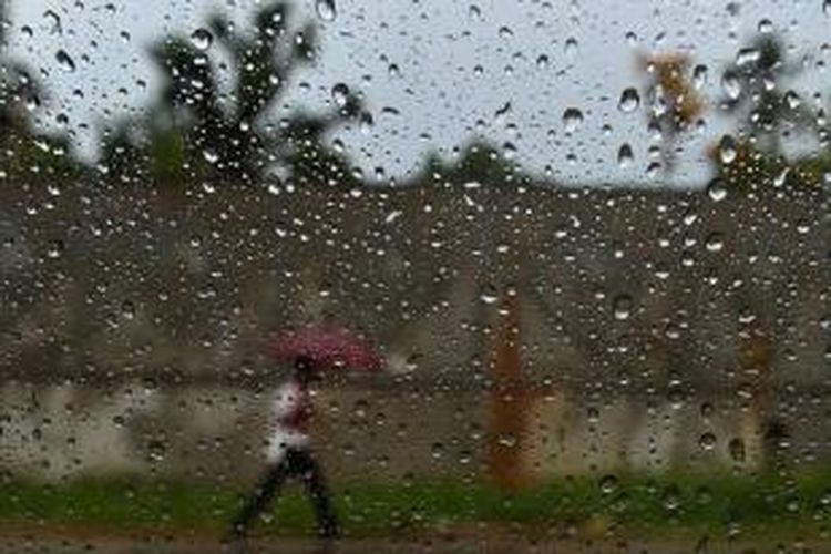 Ilustrasi: Pejalan kaki membawa payung terlihat dari jendela mobil selama hujan hujan deras.