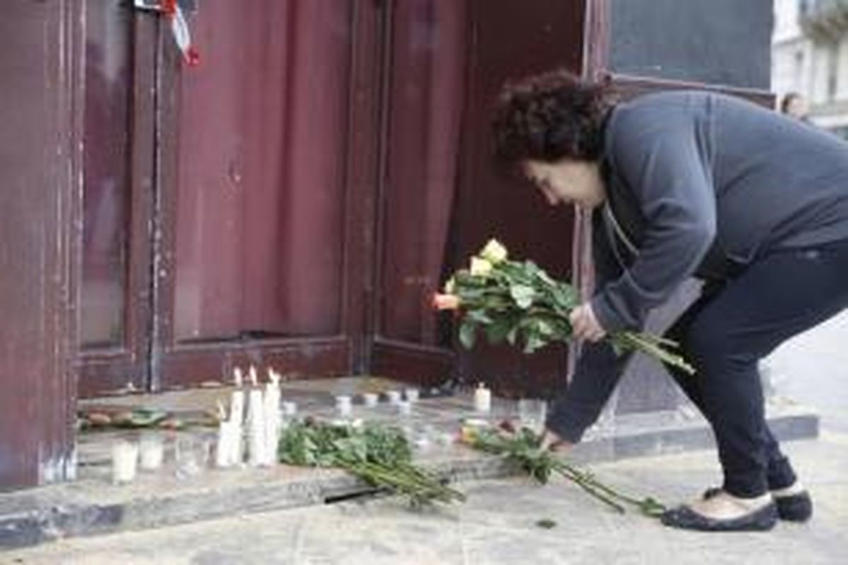 Seorang wanita meletakkan lilin dan bunga di depan bar Carillom di Paris, 14 November 2015. Lebih dari 100 orang tewas dalam aksi penembakan dan bom yang dilakukan oleh teroris pada 13 November malam.