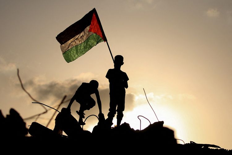 Anak pengungsi mengibarkan bendera Palestina saat berdiri di atas reruntuhan bangunan di kamp pengungsian Bureij, tengah Jalur Gaza, 22 September 2025.
