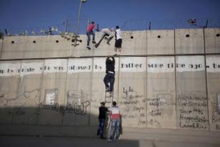 Pemuda Palestina menggunakan tangga untuk memanjat tembok pemisah Israel dalam perjalanan mereka untuk shalat di Masjid Al-Aqsa di Jerusalem, pada Jumat pertama bulan suci Ramadhan, di Al-Ram, utara Jerusalem, 19 Juni 2015. pemerintah Israel mengizinkan pria di atas usia 40 untuk mengunjungi Jerusalem selama bulan Ramadhan tanpa izin.