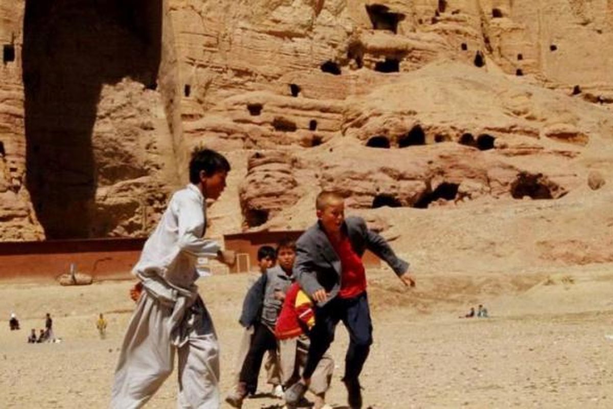 Anak laki-laki Afghanistan bermain sepak bola di depan area patung Buddha raksasa pernah berdiri di Provinsi Bamiyan, 9 April 2007. Patung-patung Buddha kuno dihancurkan oleh Taliban pada Maret 2000, meskipun ada protes internasional untuk menghentikan penghancuran.