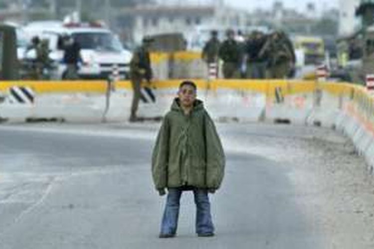 Remaja Palestina Hussam Abdo (16), seorang calon pelaku bom bunuh diri, memandangi prajurit Israel yang memamerkannya kepada media setelah dia ditangkap di dekat kota Nablus, Tepi Barat, Maret 2004. Pasukan Jihandak Israel akhirnya meledakkan bom 8 kilogram yang dibawa Abdo.