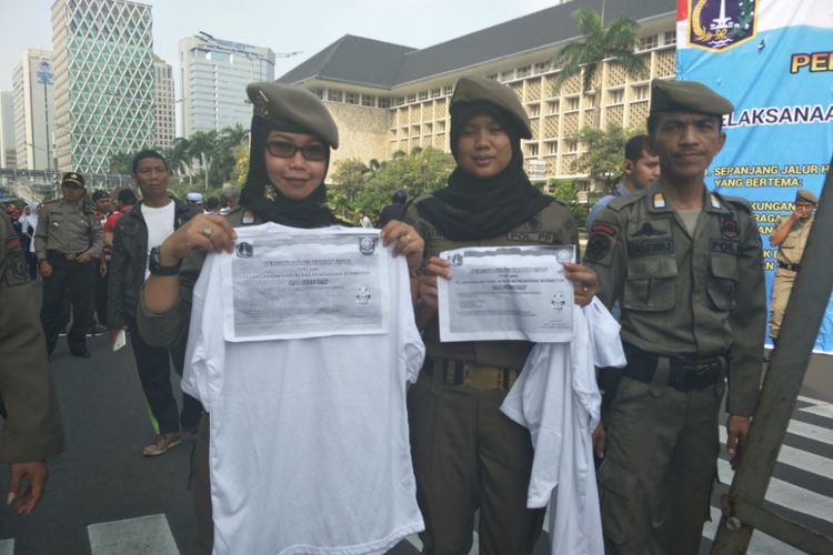 Satuan Polisi Pamong Praja (Satpol PP) DKI Jakarta membagikan kaus putih polos untuk warga yang nekat mengenakan kaus berhastag #2019GantiPresiden di kawasan Car Free Day (CFD) di Jalan Sudirman-Thamrin, Jakarta Pusat. 