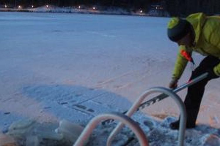 Menggergaji es untuk membuat lubang untuk berendam di tepi Danau Poikkipuoliainen, Finlandia.