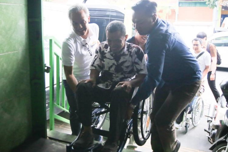 Gubernur Jawa Tengah Ganjar mengangkat kursi roda dari penyandang disabilitas saat memasuki rumah makan di Solo, Jawa Tengah, Sabtu (23/2/2019).