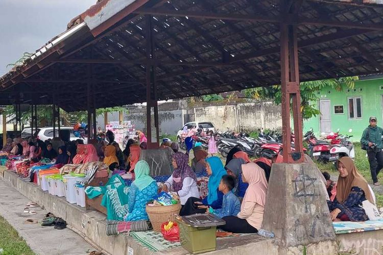 Para warga perempuan di Padukuhan Saren, Kalurahan Wedomartani, Kapanewon Ngemplak, Kabupaten Sleman saat mengikuti acara tradisi Nyadran Pasar. Mereka duduk di los Pasar Wonosari dan tepat didepanya terdapat berbagai makanan yang dibawa dari rumah untuk disantap oleh warga bersama-sama.