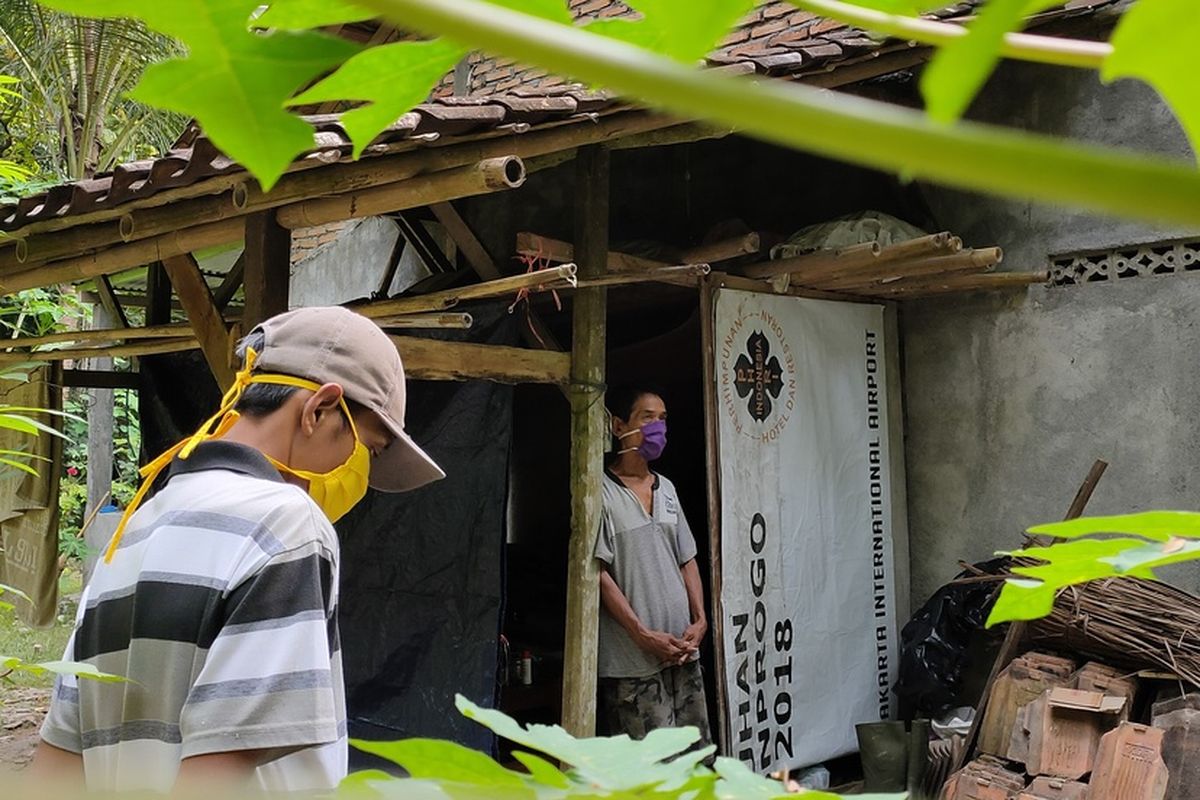 Sakir (62 tahun) pulang dari Berau, Kalimantan Timur, langsung menempati ruang isolasi dari bekas gudang kayu bakar yang berada di samping rumah. Bangunan mungil itu berada di tengah kebun kayu keras, pohon kelapa hingga jati.
