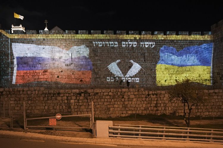 Bendera Ukraina dan Rusia ditampilkan di dinding Kota Tua Yerusalem, Minggu (13/3/2022). Tulisan dalam aksara Ibrani tersebut artinya mendoakan kedamaian, menantikan kalian.