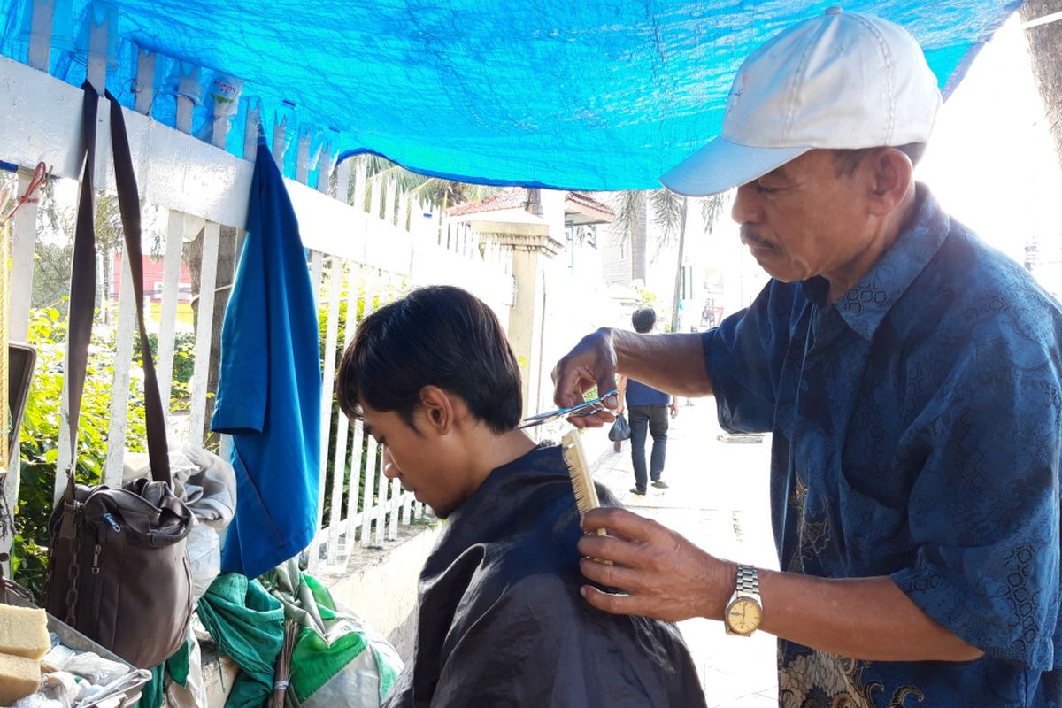 Hasan saat sedang mencukur rambut pelanggannya, Senin (11/3/2019)