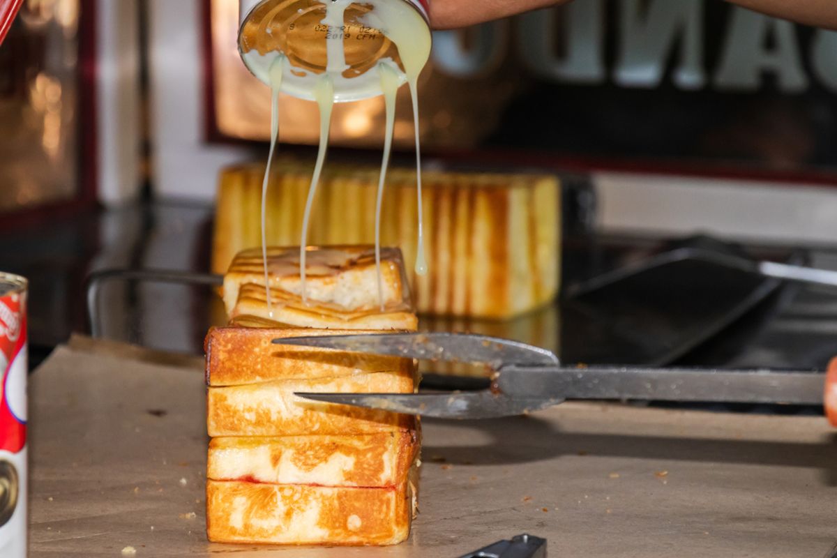 Pedagang Roti Bakar Bandung sedang menuangkan susu kental manis di roti. 