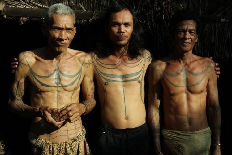Tiga pria menunjukkan tato khas Mentawai pada tubuh mereka.