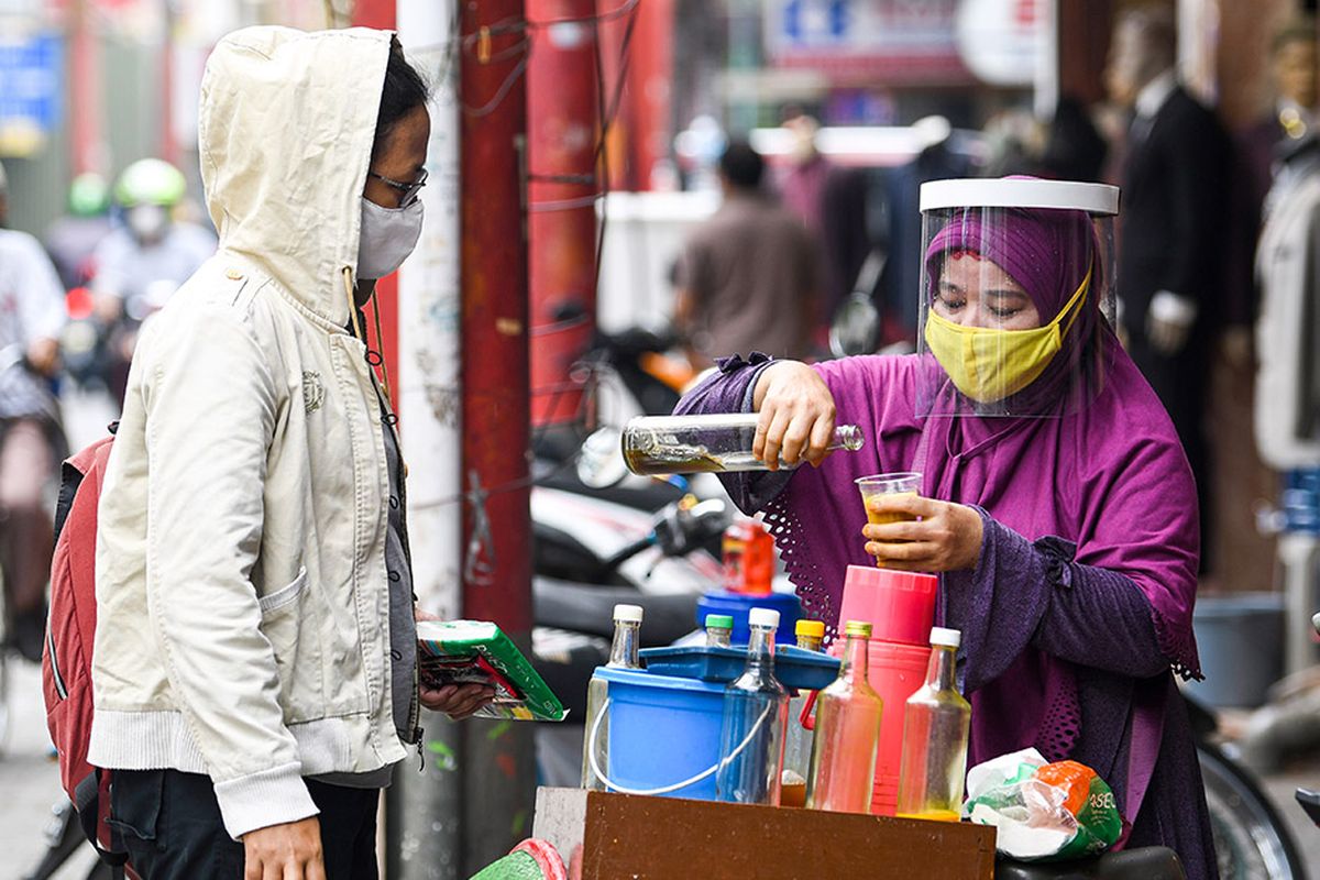 Penjual jamu keliling Tidar (kanan) dengan menggunakan masker dan pelindung wajah melayani pembeli di kawasan Pasar Baru, Jakarta, Selasa (9/6/2020). Tidar menerapkan protokol kesehatan jelang pemberlakuan protokol tatanan normal baru di Jakarta untuk tetap mencari nafkah.