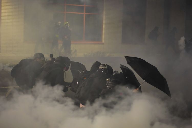 Sekelompok pedemo berlindung dengan tameng mereka dari gas air mata yang ditembakkan polisi, dalam demo pada Rabu (20/1/2021), di luar gedung Imigrasi dan Bea Cukai Amerika Serikat, Portland, Oregon.