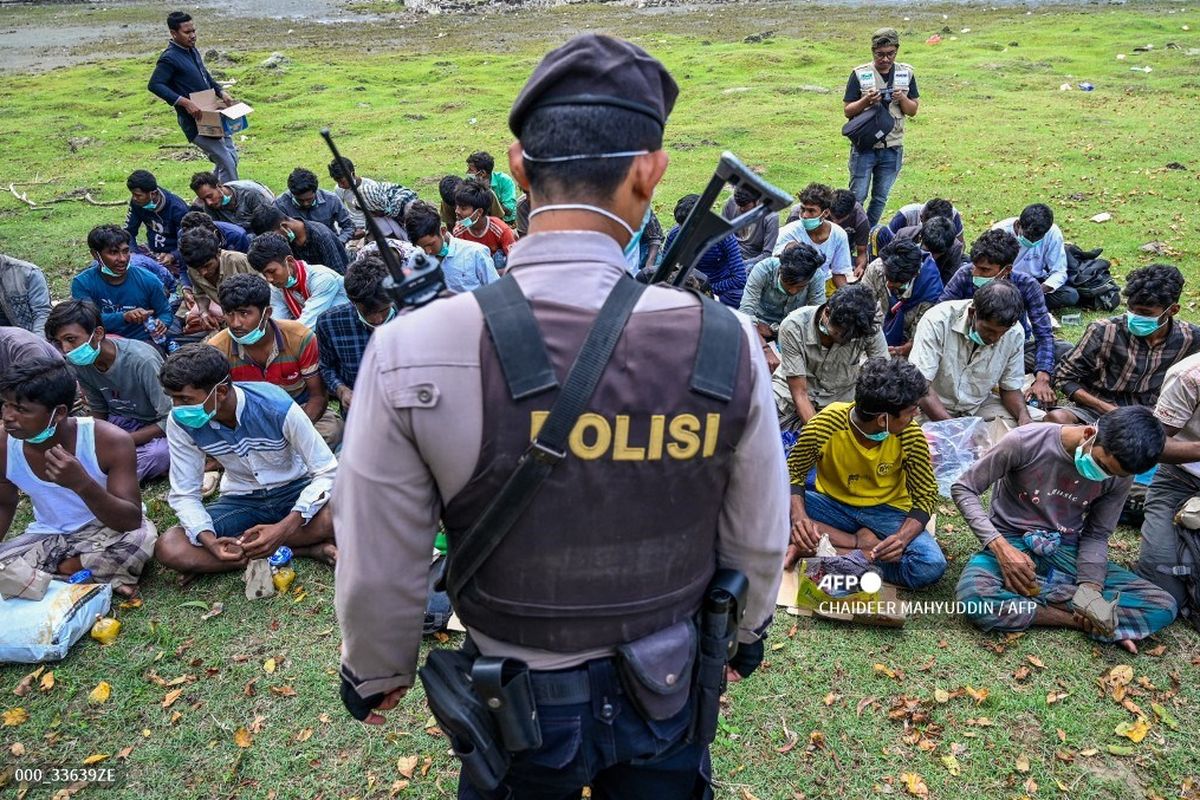 A policeman stands guard next to a group of Rohingya refugees waiting to be transferred to a temporary shelter following their arrival by boat in Krueng Raya, Indonesia's Aceh province on December 25, 2022. 