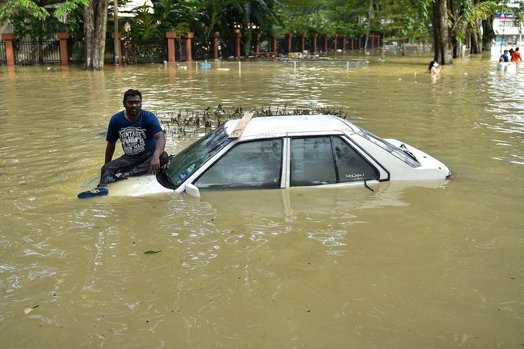 Seorang pria duduk di kap mobilnya sambil menanti dievakuasi oleh tim penyelamat di Shah Alam, Selangor, Malaysia, Senin (20/12/2021). Banjir Malaysia kali ini adalah yang terparah dalam beberapa tahun.