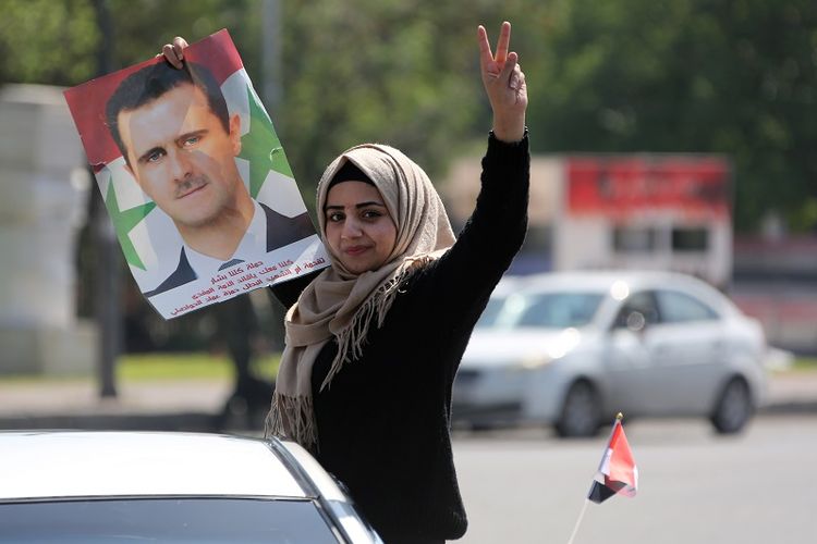 Sambil membawa foto Presiden Bashar al-Assad, seorang perempuan Suriah turun ke jalanan kota Damaskus untuk mengecam serangan udara Sekutu pada Sabtu (14/4/2018). 