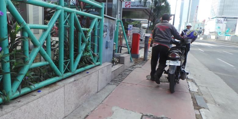 Pria ini terlihat mendorong motor di trotoar Jalan MH Thamrin, Jakarta Pusat, Rabu (17/12/2014). D jalur itu, sepeda motor dilarang melintas.