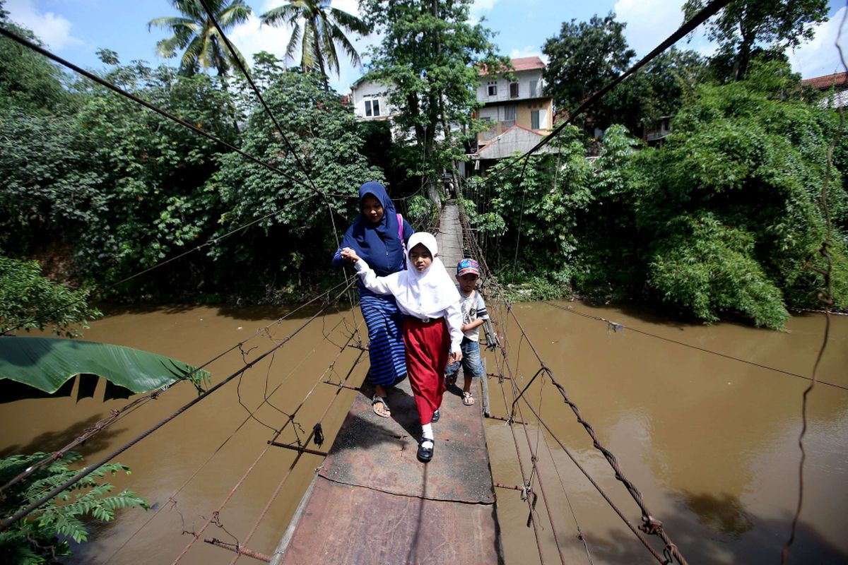 Warga menyeberang jembatan gantung di Jalan Gardu, Kelurahan Srengseng Sawah, Jagakarsa, Jakarta Selatan, Selasa (23/01/2018). Pemerintah provinsi DKI Jakarta akan segera mengeksekusi pembangunan jembatan di Jagakarsa untuk menggantikan jembatan gantung yang sudah reyot dan tak aman.