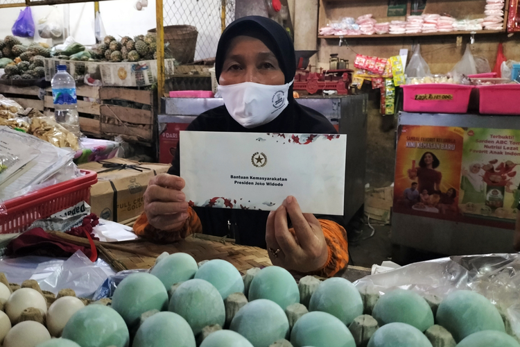 Pedagang Pasar Hardojaksino, Aminah (59) merasa senang dan menunjukkan amplop bantuan amplop putih yang bertuliskan 'Bantuan Kemasyarakatan Presiden Joko Widodo'