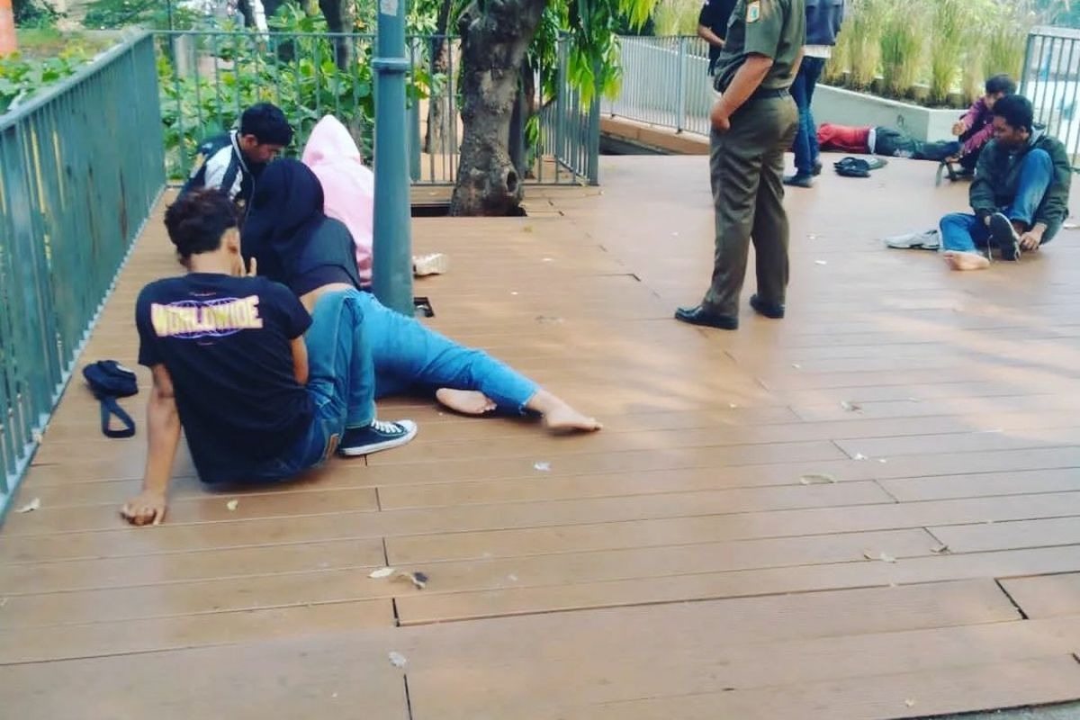 Satpol PP Jakarta membangunkan remaja yang tertidur di taman kawasan Stasiun MRT Dukuh Atas, Jakarta Pusat, Selasa (19/7/2022).