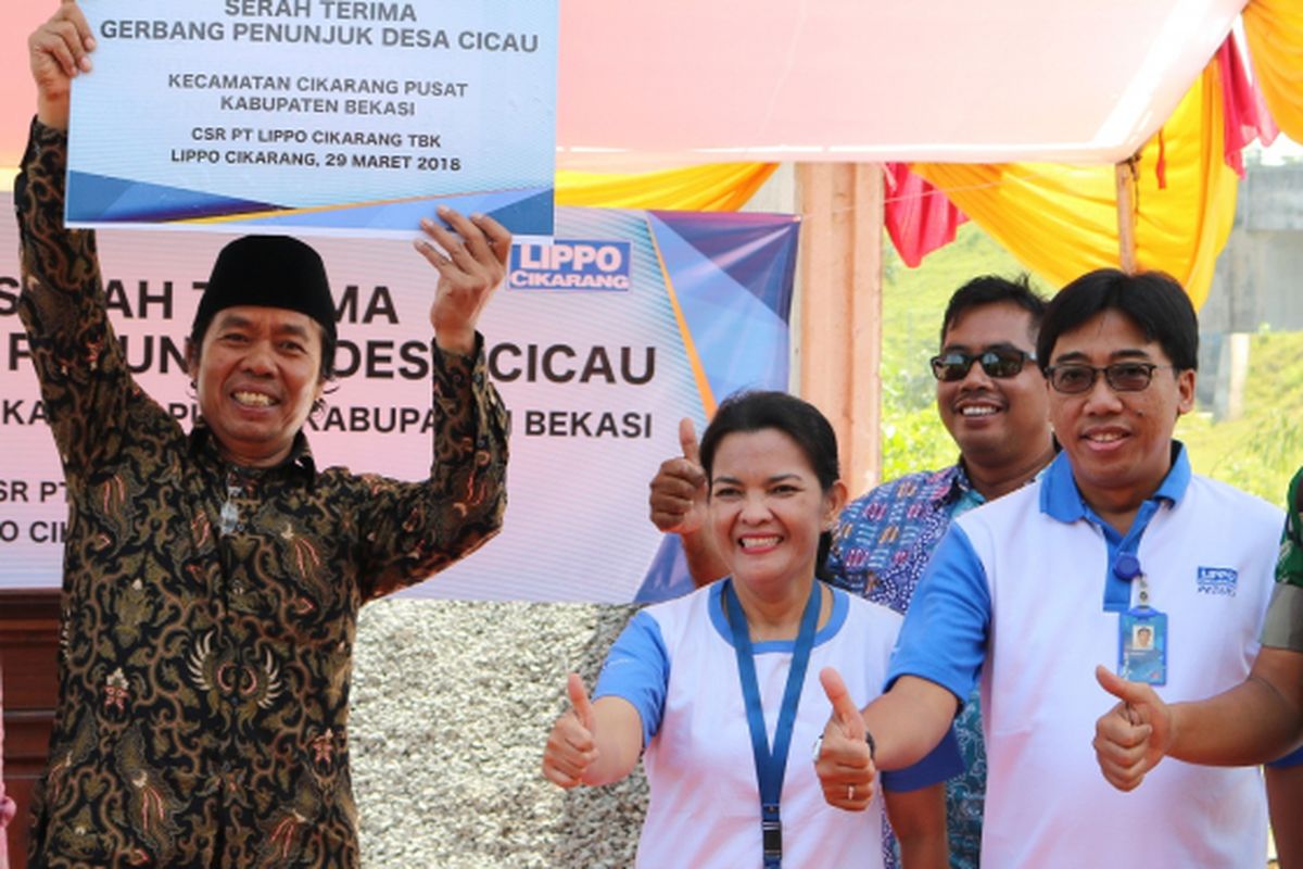 Lurah desa Cicau Kalim Maja Utama mengangkat plakat serah terima gapura yang diserahkan secara simbolis oleh Tim CSR Lippo Cikarang, Ria Sormin, di lokasi perbatasan desa Cicau dan desa Sukadami, Kecamatan Cikarang Pusat, Kabupaten Bekasi.
