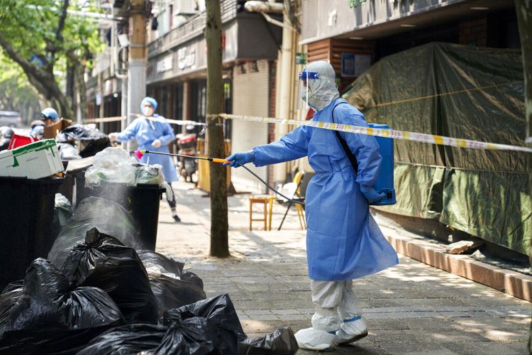 Seorang pekerja dengan alat pelindung mendisinfeksi tumpukan kantong sampah pada Kamis, 21 April 2022, di Shanghai.