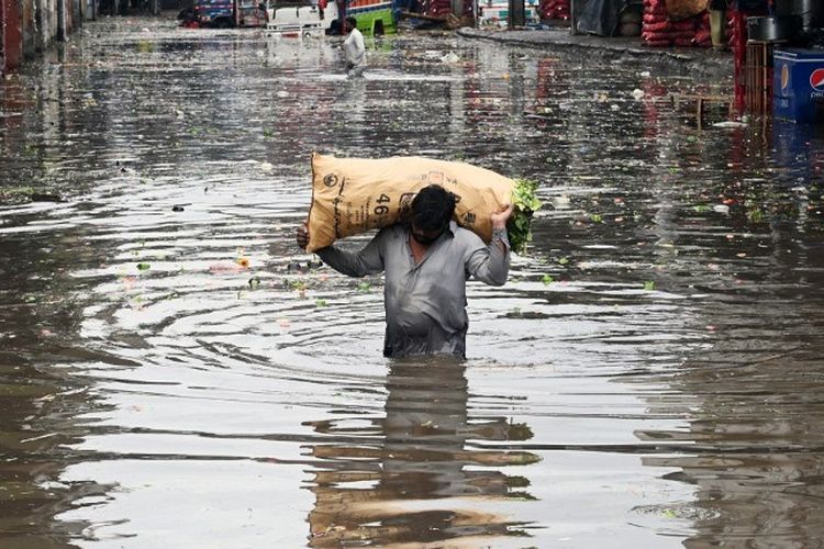 Seorang pedagang membawa karung sayuran berdaun mengarungi pasar yang terendam banjir setelah hujan deras di Lahore pada 21 Juli 2022. 