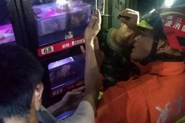 Seorang petugas pemadam kebakaran berusaha mengeluarkan tangan pria yang terjepit di mesin penjual mainan seks. Kejadian itu berlangsung di China.