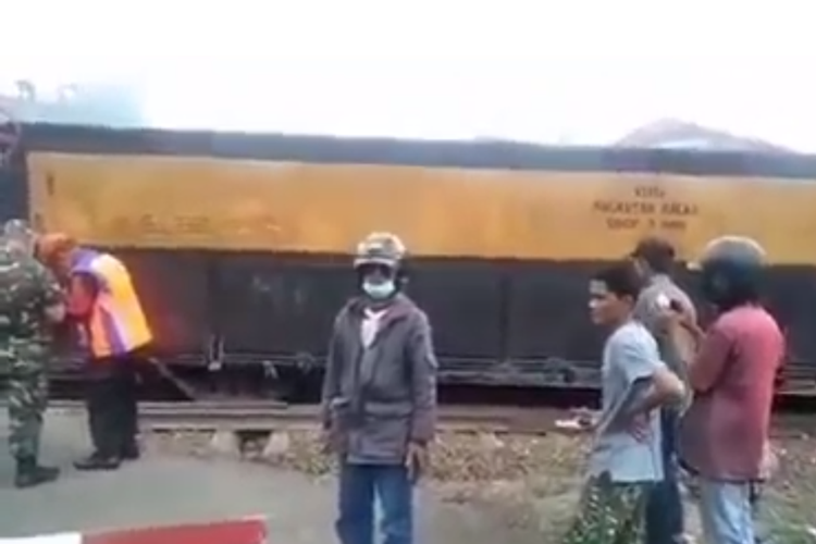 Tangkapan layar video yang memperlihatkan kereta api pengangkut batu balast anjlok di tengah perlintasan.