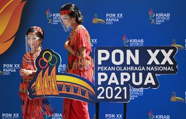 Dua warga melintas di dekat pernak-pernik PON Papua di kawasan Pasar Lama Timika, Kabupaten Mimika, Papua, Selasa (28/9/2021). Berbagai pernak-pernik PON Papua terpasang di sejumlah titik di Timika untuk memeriahkan pagelaran olah raga nasional empat tahunan tersebut.  ANTARA FOTO/Aditya Pradana Putra/tom. 
