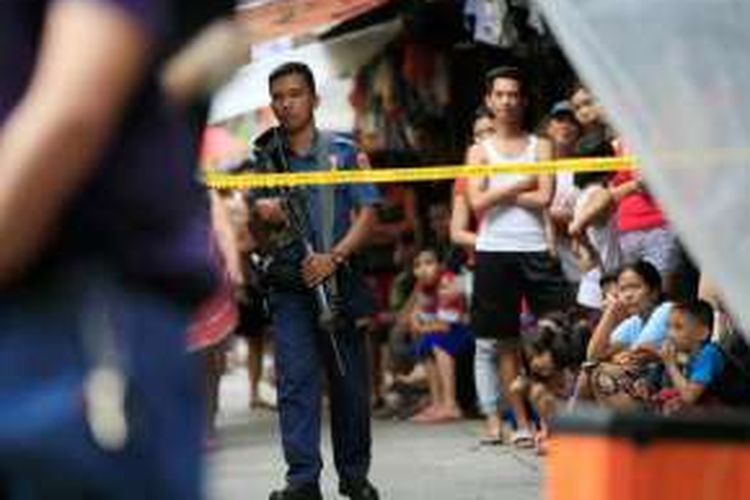 Seorang anggota Kepolisian Nasional Filipina (PNP) berdiri memegang senapan serbu mengawasi warga yang ikut mengerubuti tempat kejadian perkara penembakan dua tersangka pengedar narkoba dalam operasi polisi di Metro Manila, Filipina, 8 Oktober 2016.