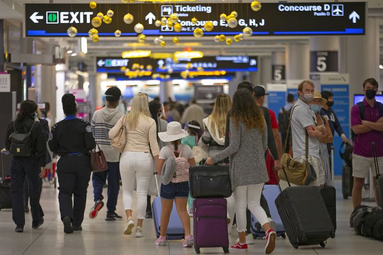 Para penumpang memakai masker saat menuju Concourse D di Miami International Airport pada Minggu (22/11/2020). Bandara-bandara di Amerika Serikat mencatat lonjakan penumpang jelang perayaan Thanksgiving yang jatuh pada Kamis (26/11/2020).