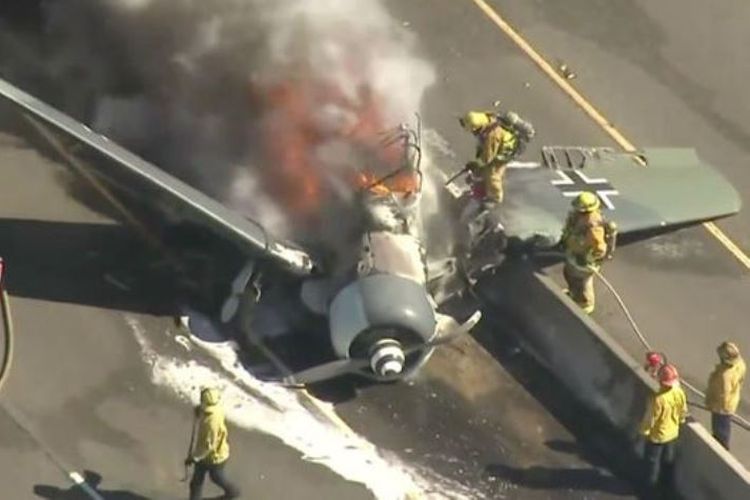 Petugas pemadam kebakaran saat berupaya memadamkan api yang membakar badan pesawat AT-6 yang jatuh di jalan tol di California.
