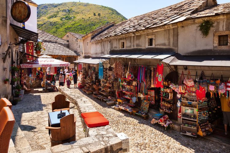 Jalanan di Old Town Mostar dengan latar belakang gunung dan jejeran toko suvenir serta kafe