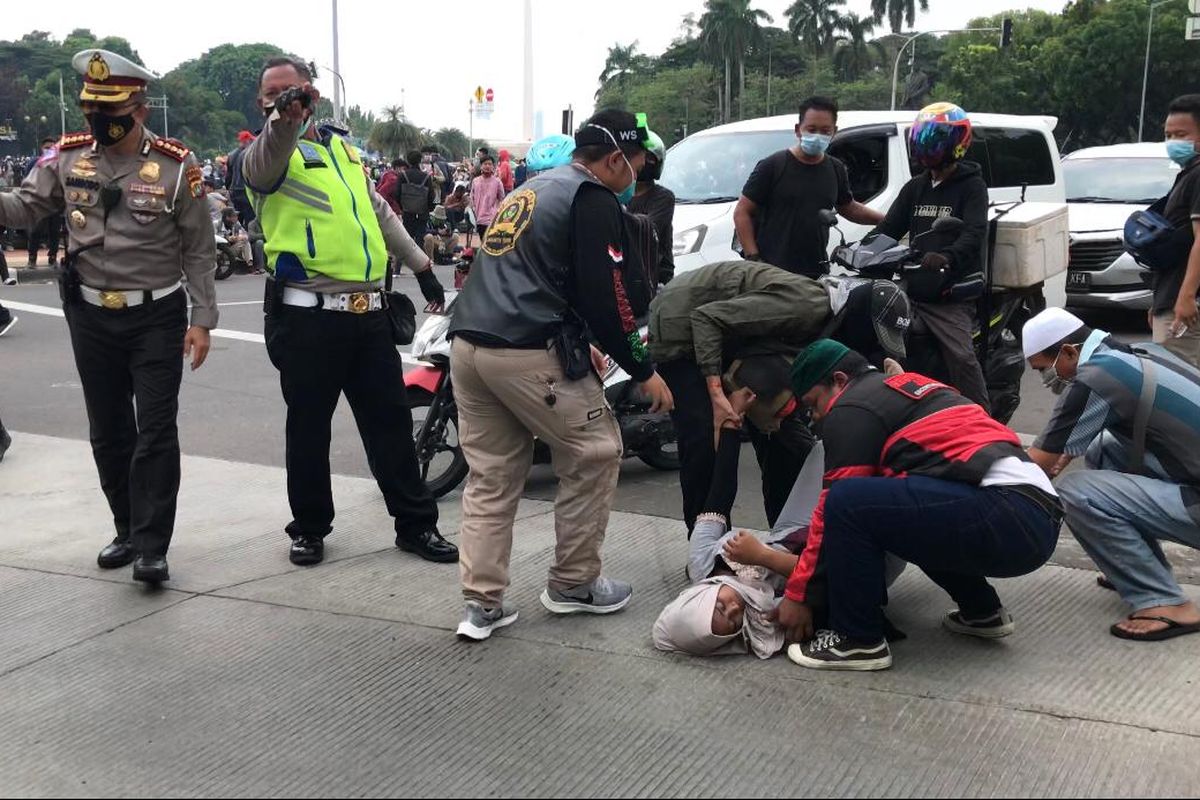 Seorang perempuan jatuh pingsan saat sedang berjalan kaki di tengah kerumunan massa dekat bundaran Monas, Rabu (13/10/2020). Tak jauh dari lokasi, massa tengah berunjuk rasa menolak UU Cipta Kerja.