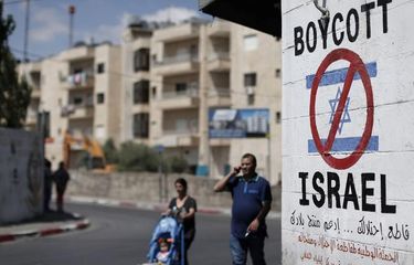 Warga Palestina berjalan di dekat sebuah tanda di tembok Bethlehem yang menyerukan untuk memboikot produk Israel.