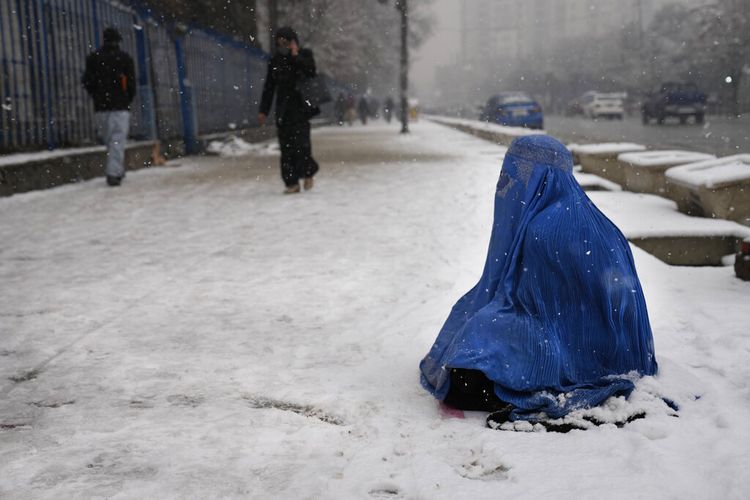 Seorang wanita Afghanistan mengenakan burka, kanan, memohon di atas salju di Kabul, Afghanistan, Minggu, 6 Februari 2022. 